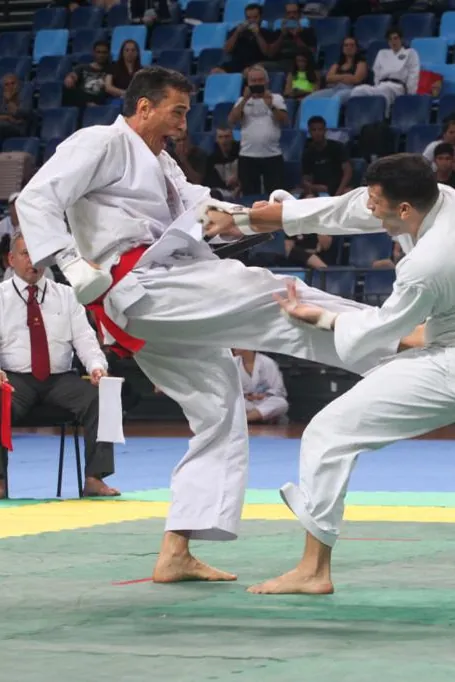 Jayme Sandall chuta numa luta de kumite em campeonato, com os árbitros ao fundo